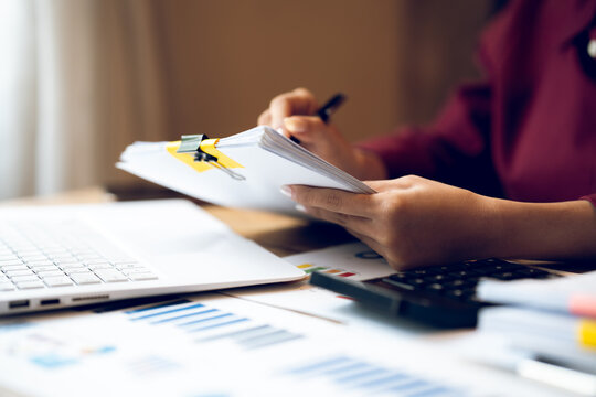 Business professional working on a laptop with financial charts, calculator, documents and coffee on a wooden desk, representing finance, accounting and office work.