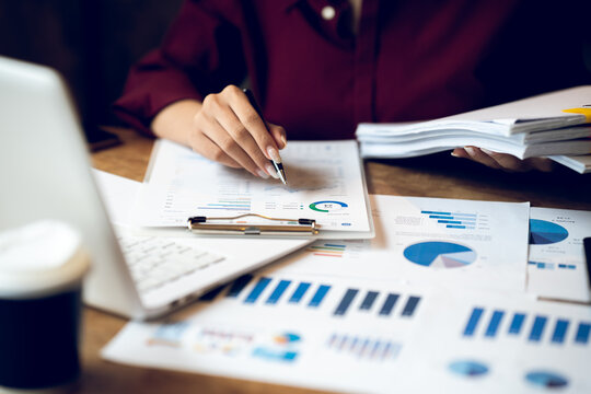 Business professional working on a laptop with financial charts, calculator, documents and coffee on a wooden desk, representing finance, accounting and office work.
