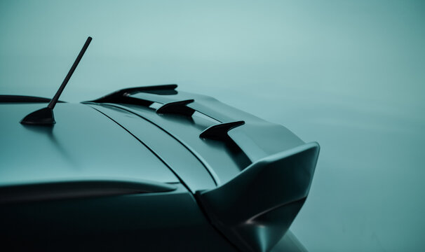 Rear spoiler on black car against bright teal background. Aerodynamic element on the top of car rear hatch for reducing lift.
