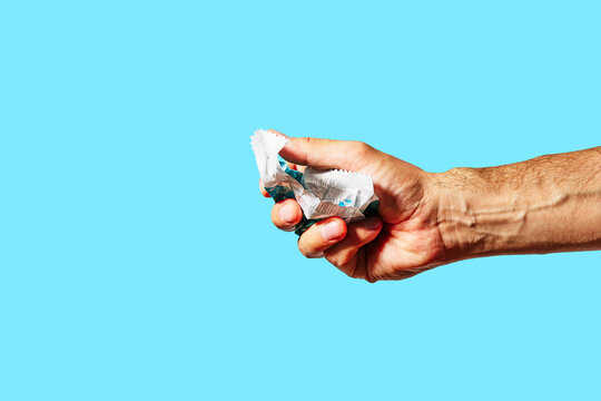Hand Holding Crumpled Candy Wrapper on Blue Background