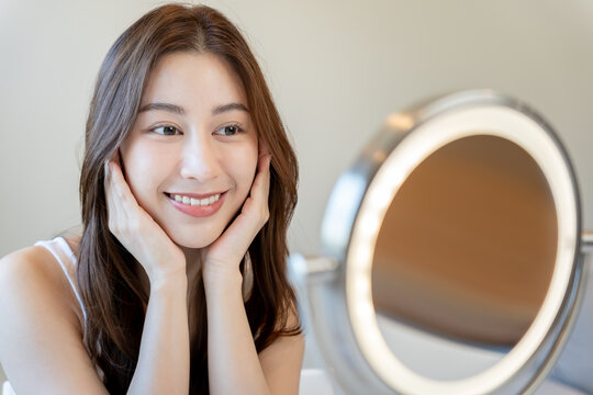 Beautiful Asian woman sit in front of a mirror. face of a healthy woman smile for good skin care. Advertisement for skin care, anti-wrinkle, baby face, whitening, moisturizer, tighten pores serum