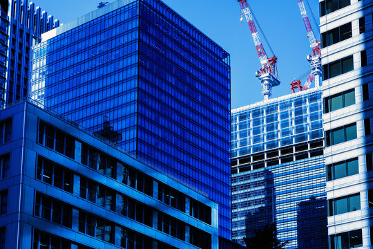 Modern skyscrapers and construction tower cranes building new office architecture in Tokyo business district under blue sky.