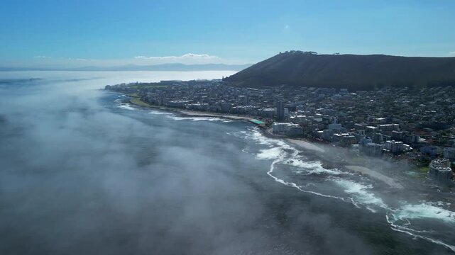 Fog is coming in from the Atlantic to Cape Town South Africa Blue sky - waves on the beach - aerial drone view
