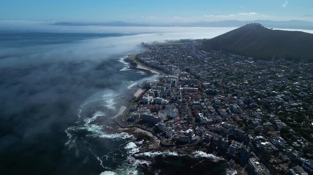 High altitude aerial drone view over Cape Town South Africa , Fog is coming in Signal Hill in the background little tilt and backwards flight , waves crushing on the beach