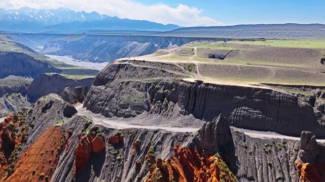 Aerial view of a flock of sheep and a vehicle on a winding dirt road along the edge of a deep colorful canyon in Anjihai Grand Canyon, Xinjiang, China