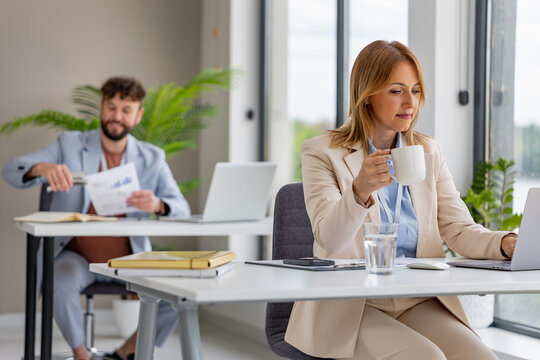 Woman working on laptop while man sits at desk in modern office space during daytime