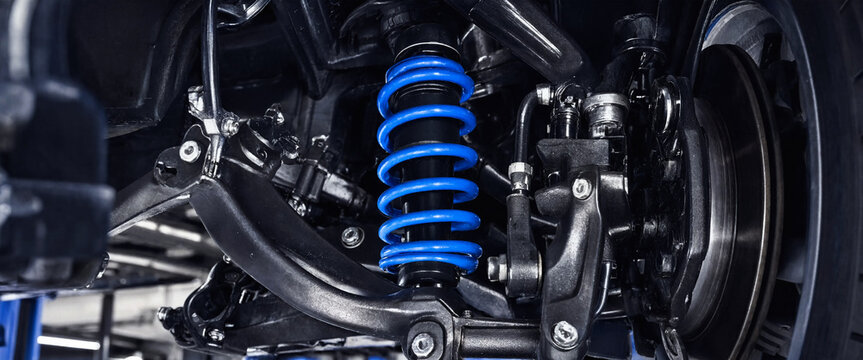 Close up of a blue car suspension coil spring and chassis components in a workshop.