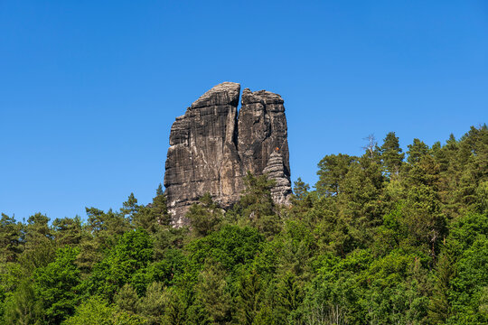 A large rock formation rises above a green forest in Germany