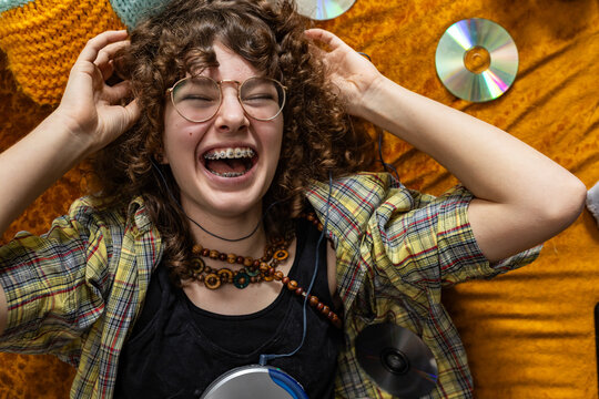 A laughing teenage girl enjoys music with compact discs indoors