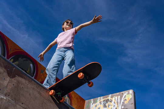 Smiling teenage girl rides a skateboard on an outdoor ramp