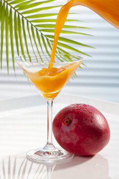 Mango juice being poured in martini glass besides mango