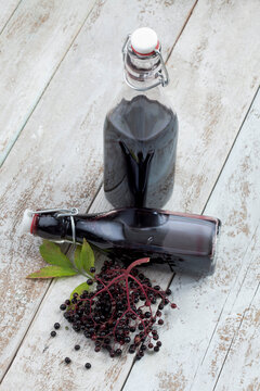 Elderberries (Sambucus) and two bottles of elderberry juice on white wooden table, studio shot
