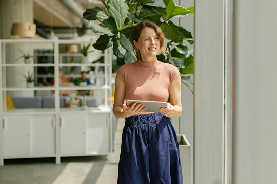 Smiling businesswoman holds a digital tablet in a modern sunny office