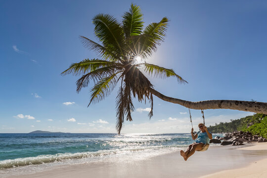Seychelles, La Digue, Anse Fourmis, beach with palm and tourist on swing