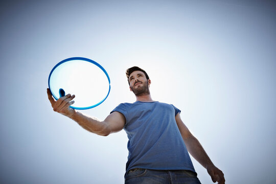 Man holds a blue frisbee outdoors against the clear sky