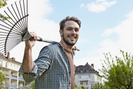 Germany, Cologne, Portrait of young man holding rake, smiling