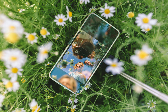 Friends take a joyful smartphone selfie in a chamomile meadow