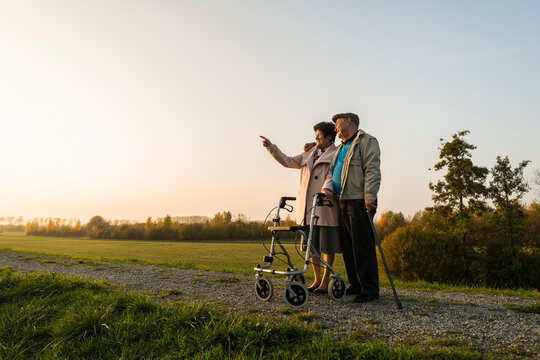 Senior couple with walking stick and wheeled walker standing in the nature