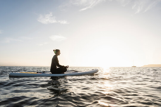 Young woman meditating on paddleboard at sunset