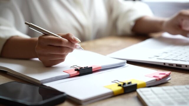 Business professional working on a laptop while managing stacks of organized documents and paperwork in a bright modern office.