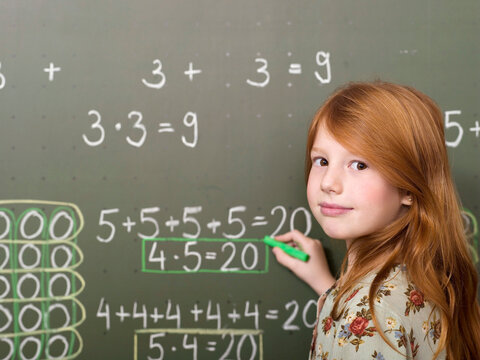 Girl (6-7) standing and writing on blackboard, portrait, close-up
