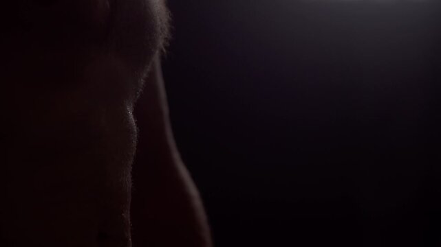 Macro close up of male abs shaking from extreme muscle tension and exhaustion. Athletic shirtless man flexing core muscles in dark low key studio.