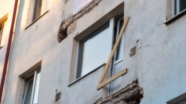 Residential building exterior showing significant facade damage, exposed brickwork, crumbling plaster, structural defect evidence, urgent repair needed, visible disrepair, city infrastructure problem.