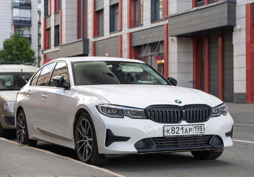 White luxury modern BMW 3 series G20 sedan car parked on an urban street side near old brick building facade, exterior view of premium german vehicle, executive transport business auto. German car. 
