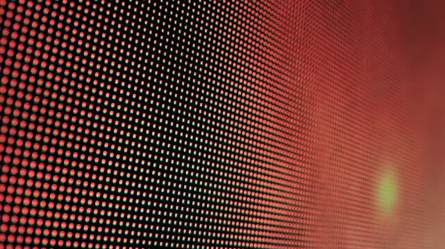 Close-up perspective of LED screen pixels displaying vibrant red and orange light pattern, abstract digital technology background with dynamic glowing dots, slow motion