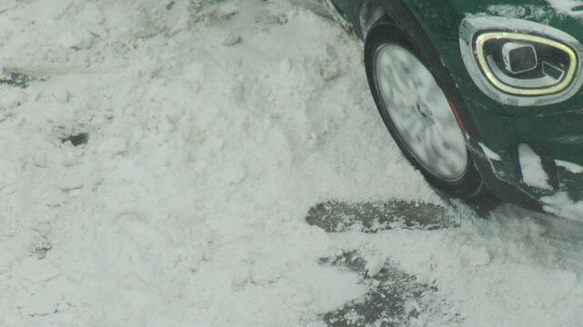 Car wheel spinning in deep snow during winter conditions, vehicle stuck in snowdrift, attempt to clear path on snowy road, slow motion