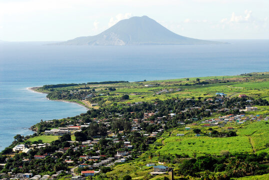 Saint Kitts, the green plain of Saint Kitts, with a small city, on the shores of the caribbean sea, and the volcano of the Netherlands' owned Sint Eustatius Island in the background