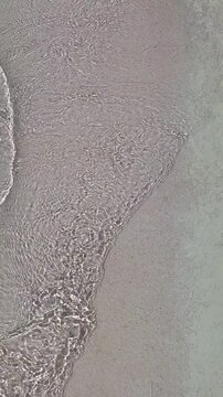 Sand and water meet on the shore as waves roll in during a sunny afternoon 