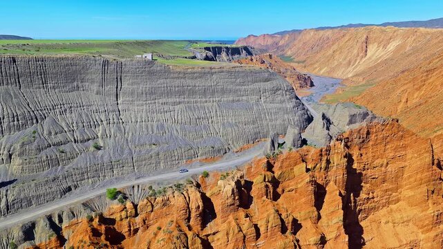 Aerial view of a remote dirt road on a steep eroded canyon cliff with a vehicle driving in a rugged mountain landscape in Anjihai Grand Canyon, Xinjiang, China