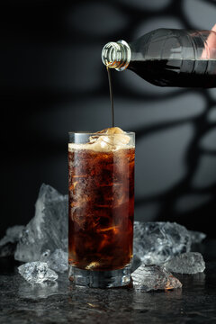 Cola is poured into a glass with ice.