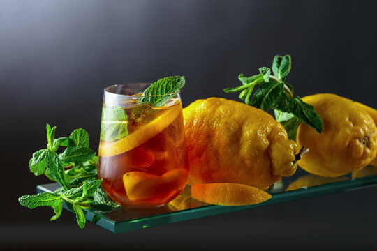 Misted glass of iced tea with fresh lemons and mint branches on a black background.