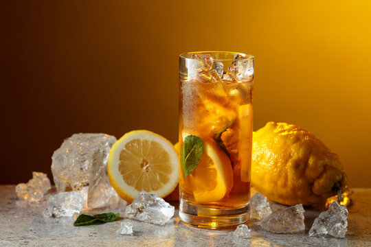 Classic iced black tea in tall glass with lemon wedges, ice cubes and mint leaves.