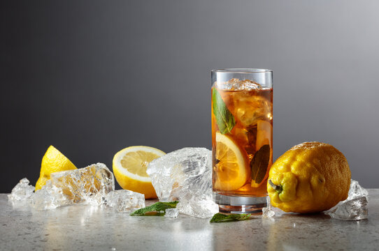 Classic iced black tea in tall glass with lemon wedges, ice cubes and mint leaves.