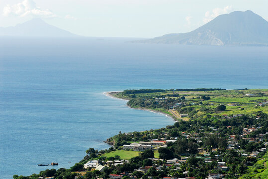 Saint Kitts, the green plain of Saint Kitts, with a small city, on the shores of the caribbean sea, and the volcano of the Netherlands' owned Sint Eustatius Island in the background