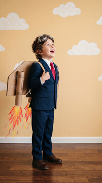 Boy in suit with cardboard rocket pack and aviator goggles, symbolizing imagination, ambition, and childhood dreams of flight.