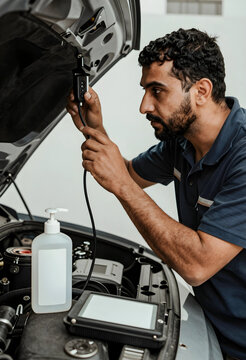 Automotive mechanic performing car engine diagnostics with specialized equipment and a tablet in a garage, the professional technician is focused on inspecting the vehicles motor