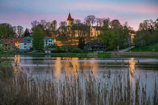 Scenic dawn over Talsi town in Latvia with church and lights reflecting in lake water, view through dry reeds