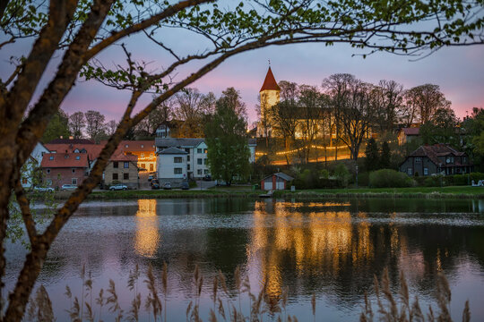 Scenic dawn over Talsi town in Latvia with church and lights reflecting in lake water, framed by tree branches