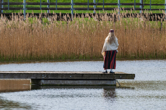 Woman in Latvian traditional folk costume standing on wooden pier by lake in Talsi Latvia
