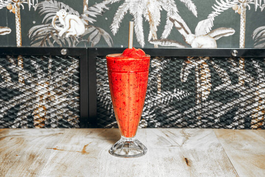 Red Fruit Smoothie in Fluted Glass Set Against Black-and-White Jungle Wallpaper