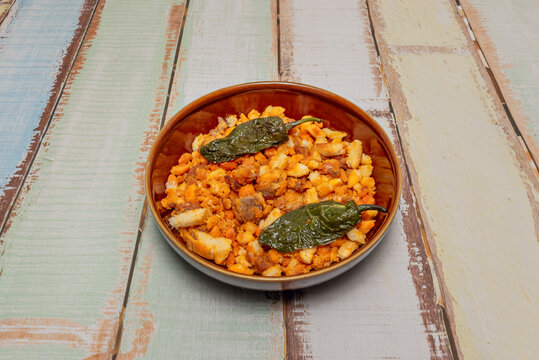 Bowl of traditional Spanish migas topped with fried green peppers on rustic weathered wooden table