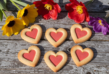 Fototapeta premium Heart shaped cookies with red centers and colorful spring flowers on a rustic wooden table