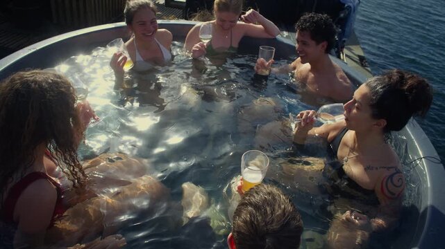Group fun as friends enjoy drinks in an outdoor hot tub by the water