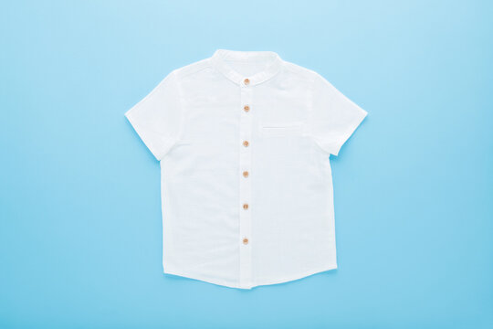 Ironed white classic short sleeved shirt on light blue table background. Pastel color. Closeup. Clothes for little child boy. Flat lay. Top down view.