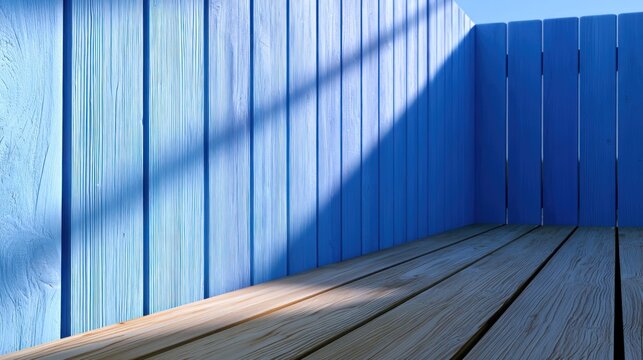 Sunlit blue wooden fence corner casts a striking shadow on wooden deck floor under clear skies