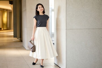 Fototapeta premium チャコールトップとアイボリーの立体スカートで歩く商業施設の女性